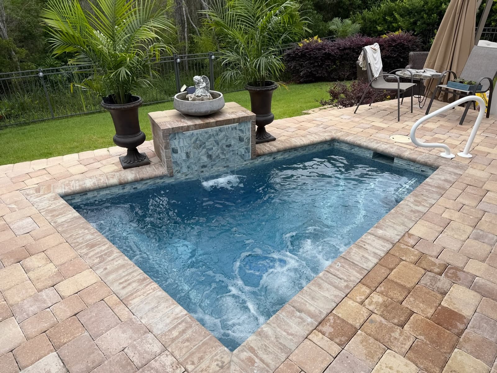 Pool with a fountain pedestal and spa jets running, set in a paver deck